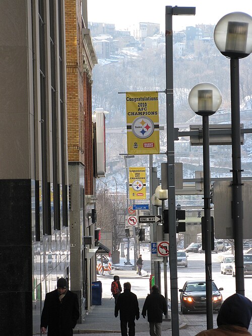 A downtown sidewalk at Court Place off Grant Street, street lamps and a one way sign, the South Side hillside visible past an elevated roadway.