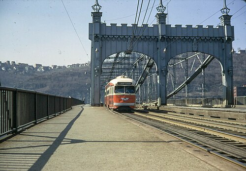 The Smithfield Street Bridge's lenticular steel truss, arched portals with castellated tops, a streetcar crossing on the near track.