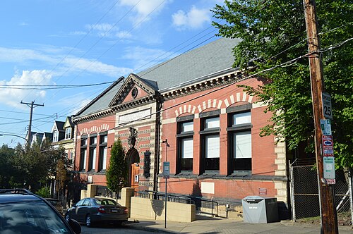 The red brick and stone Carnegie Library branch on Fisk Street, set on a sloping street with trees and parked cars.