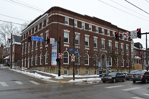 A four storey brick corner building on Butler Street with arched ground floor windows, leasing banners on the front, snow on the ground.