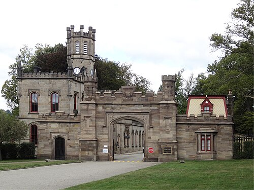 A cut stone gatehouse with a clock tower and castellated parapets at the Butler Street entrance to Allegheny Cemetery.