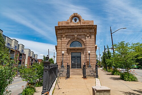 A stone bank building on Butler Street with an arched entryway and iron fencing along a wide sidewalk.