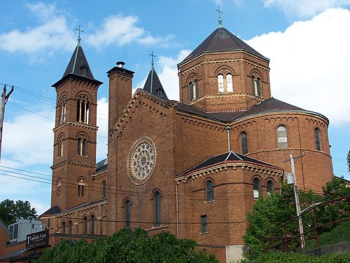 A large brown brick Romanesque Revival church with towers, spires and a rose window against the sky.