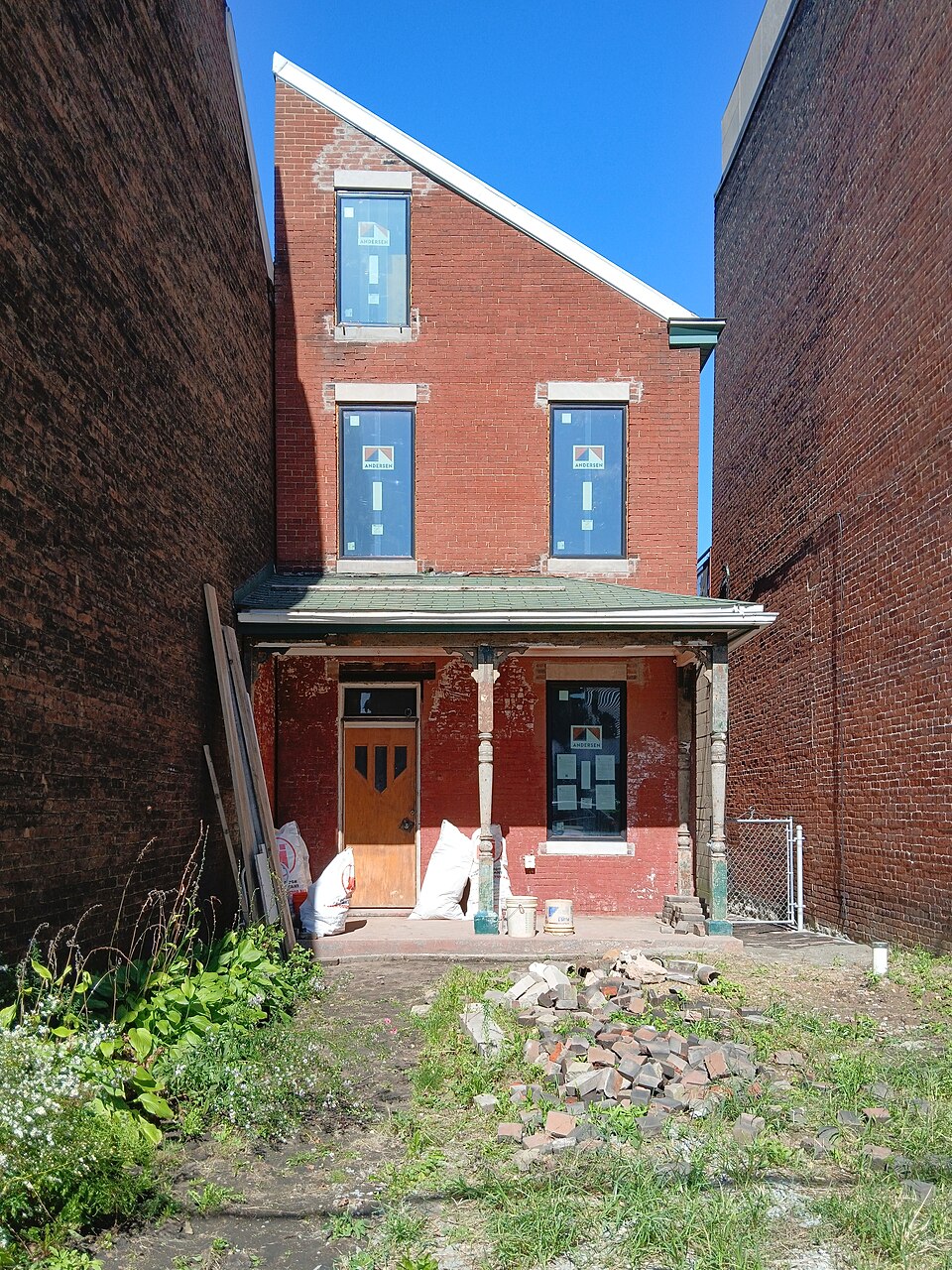 A narrow red brick building under renovation, three storeys, tucked between two taller brick side walls with debris out front. The kind of narrow brick building along these blocks rather than the actual apartment above the corner at Butler and Fisk, a few streets over on Penn Avenue rather than Butler Street.
