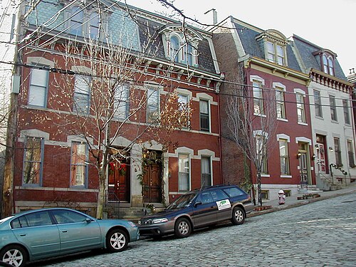 Buena Vista Street, red brick rowhouses with mansard roofs and dormered attics, a sett paved roadway in the foreground and a fire hydrant at the curb.