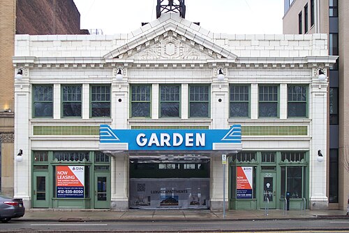 The Garden Theater's Beaux Arts front elevation in daylight, a white terra cotta pediment and cornice over green painted storefronts and a blue marquee reading Garden.