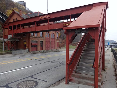 A red steel pedestrian bridge crossing the street to the Duquesne Incline's other station, a two storey red brick building.