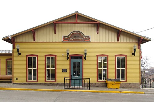 The Monongahela Incline's upper station on Grandview Avenue, yellow wood siding, dark red trim, a glass door and a sign over the entrance.