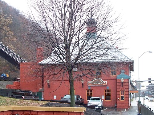 The Monongahela Incline's 1904 lower station, red brick behind a bare tree, the track climbing the hill directly behind it.