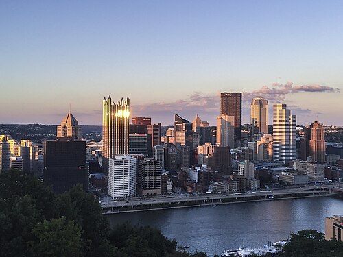 The downtown skyline across the river at sunset, seen over the treetops from the ridge.