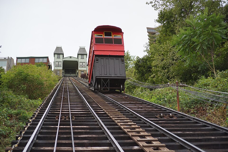 A red incline car climbing the steep wooden track up the hillside, green trees and foliage on both sides.
