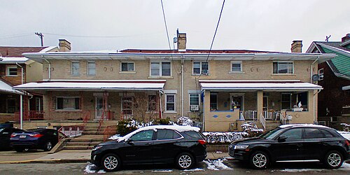 A two storey tan brick duplex on Coltart Avenue, with a low hip roof, a front porch and cars parked along the curb.