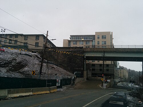 An overpass on Forbes Avenue with a stone retaining wall and institutional buildings behind it in winter.