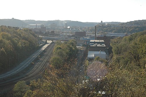 The rail valley between Polish Hill and Lawrenceville, freight tracks running below a wooded slope with industrial buildings along the corridor.