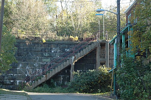Concrete city steps climbing beside a stone retaining wall and a wood-frame house, a Bigelow Boulevard street sign at the top.