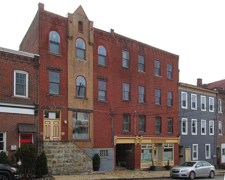 A tall narrow red brick commercial building on Brereton Street with a storefront under a striped awning at ground level, arched window heads and a stone stoop next door.