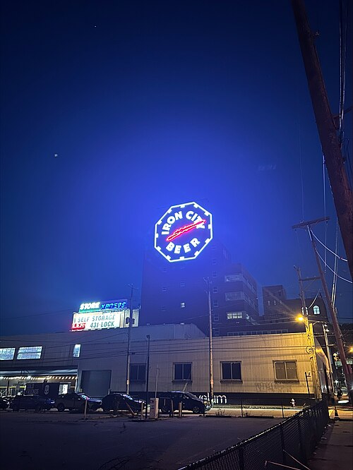The Duquesne Brewery Clock lit blue at night, an Iron City Beer face sixty feet across above a corrugated metal warehouse.