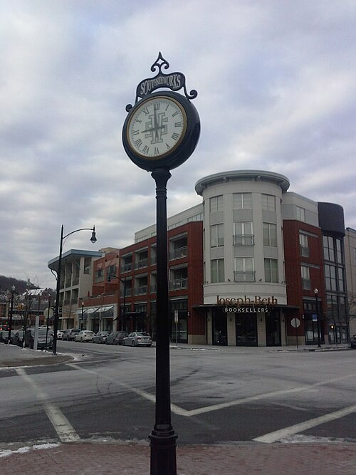 A post clock reading SouthSideWorks in front of a modern brick and glass retail building with apartments above.