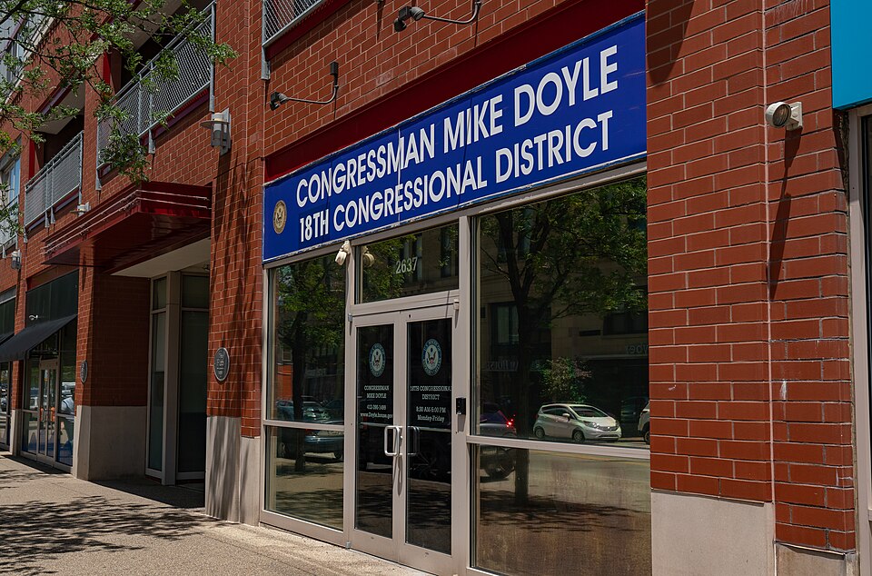 A red brick storefront at 2637 East Carson Street with glass double doors and a blue awning sign, street trees reflected in the windows.