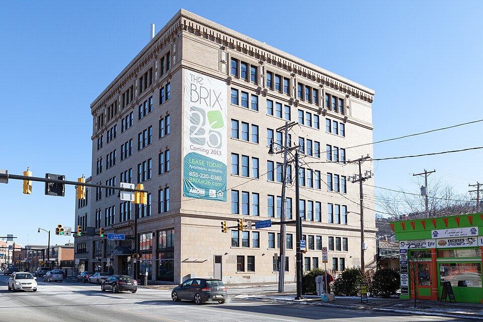 The Pittsburgh Mercantile Building at Carson and South 26th Street, a seven storey tan brick corner building with storefronts and traffic signals below.