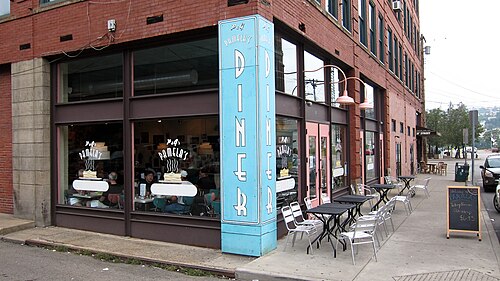 Pamela's Diner on a brick corner, a blue neon sign reading Diner, sidewalk tables and chairs, and a 21st Street sign visible down the block.