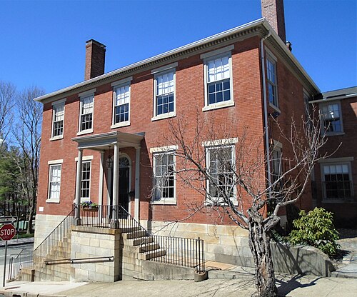 A two storey red brick Federal house on a granite foundation, with a columned entrance porch and a short flight of brick and stone steps to the sidewalk.