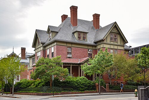 A three storey Queen Anne house in red brick and shingle with cream trim, a patterned slate roof, tall brick chimneys and gabled dormers, on a Brown University side street.