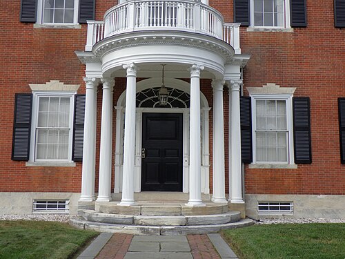 A symmetrical red brick Federal mansion with a white columned entrance porch, granite steps and an iron handrail.
