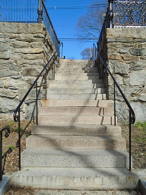 A granite staircase climbing the hill between stone retaining walls, with wrought iron handrails on both sides.