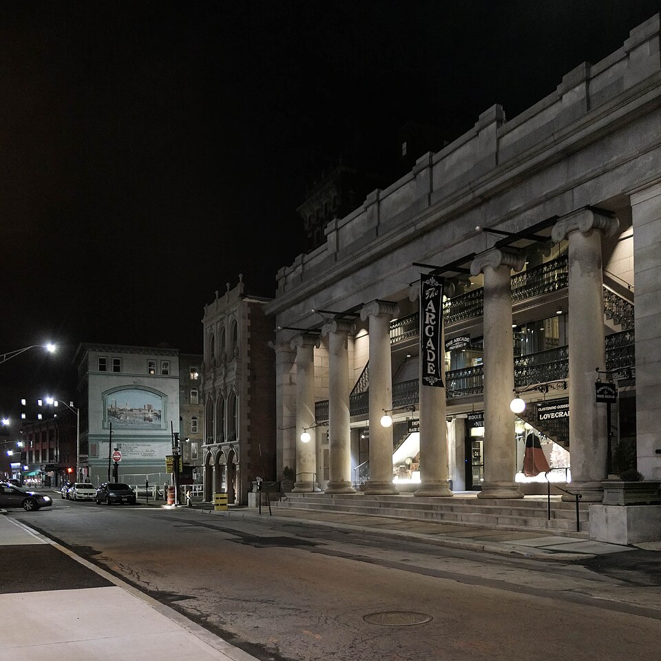 The Arcade's colonnaded entrance on Westminster Street at night, six columns under a stone pediment, a banner reading The Arcade hung between them, and an iron balcony visible through the colonnade.