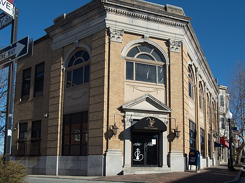 A two storey tan brick corner building on Atwells Avenue with arched upper windows, corner pilasters and black door awnings, built for Heritage Loan and Investment.