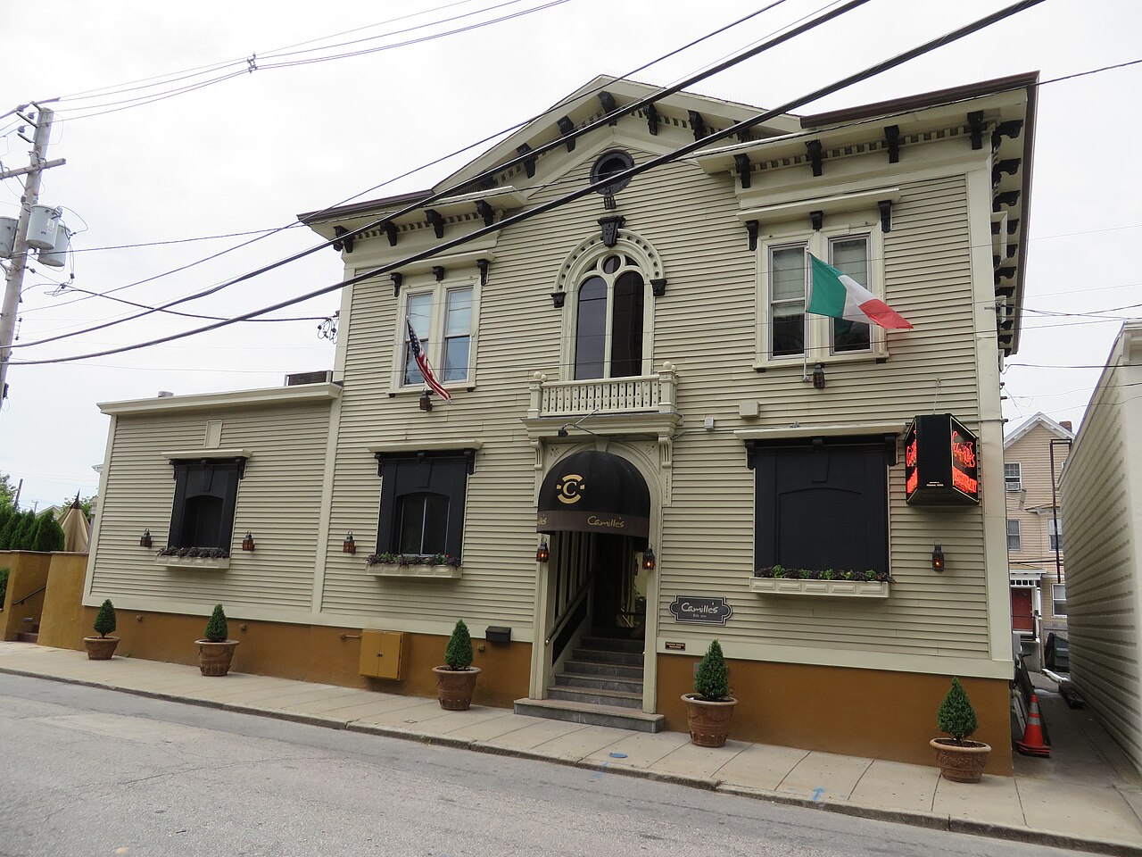 A two storey beige clapboard restaurant on Bradford Street, black entrance awning, decorative window frames and potted plants along the sidewalk.