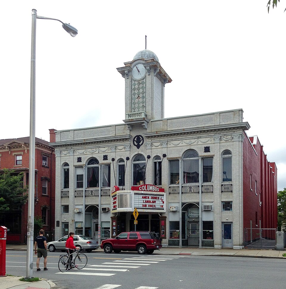 A white tiled theatre building on Broadway with a central clock tower marquee and double height arched windows.
