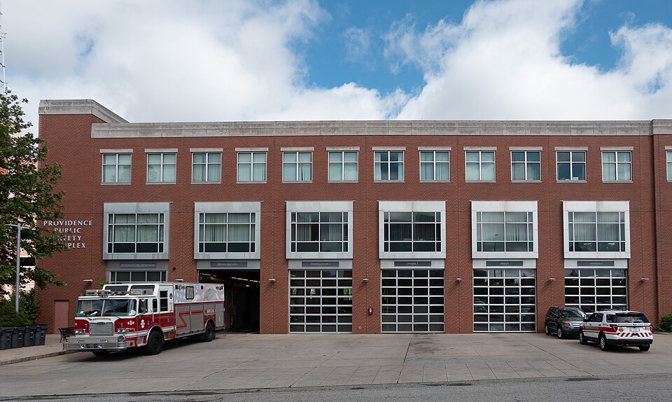 A three storey red brick Public Safety Complex on Washington Street, fire station garage bays and parked emergency vehicles out front.