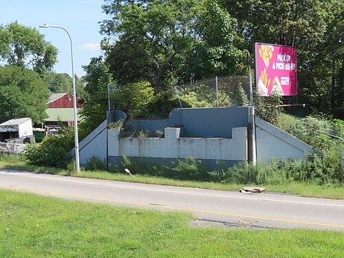 A concrete railroad bridge abutment along an asphalt road, chain link fencing beside it.