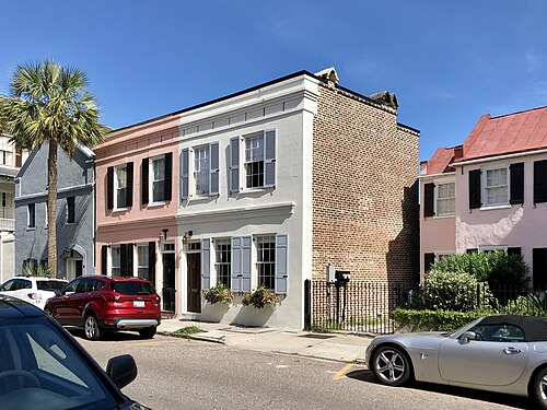 A two storey corner building in pink and white stucco over a brick side wall, with a palmetto out front and cars parked at the kerb.