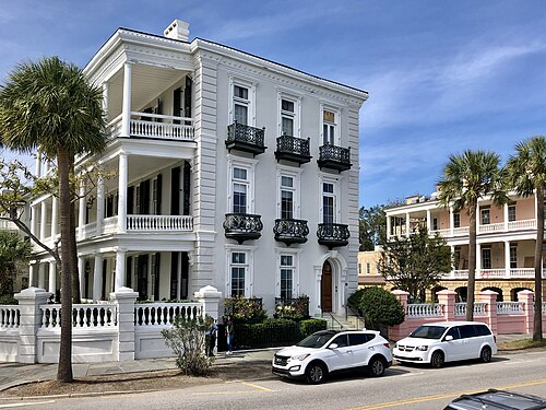 A three storey white mansion at East Battery with wrought iron balconies on every floor and palmettos along the fence.