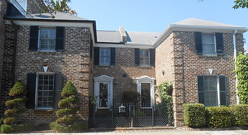 A pair of brick rowhouses with black shutters and dentil cornices, a small walled courtyard behind wrought iron gates.