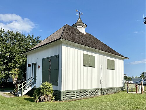 A small white board-and-batten boathouse with a hipped shingle roof, a weathervane cupola and green shutters, at the old Coast Guard station.