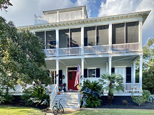 A white two storey officer's house with screened double porches, a red front door and an American flag, address plate reading 1724.