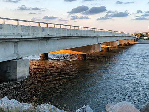 A low concrete bridge over Breach Inlet connecting the island to Isle of Palms, beach houses visible along the shore at sunset.