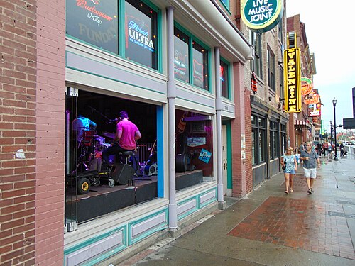 The front of the Tin Roof at 316 Broadway with the window lifted open to the sidewalk, a band playing on a platform just inside and the Valentine's vertical sign further up the block.