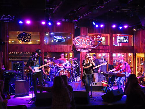 Inside The Stage on Broadway at 412, a five piece band under the venue's neon sign and a rig of purple and blue wash lights.