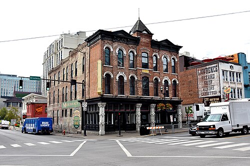 Merchants at 401 Broadway on the corner of Fourth Avenue, a brick Queen Anne building with arched windows, a corner turret and a painted DRUGS sign along the cornice.
