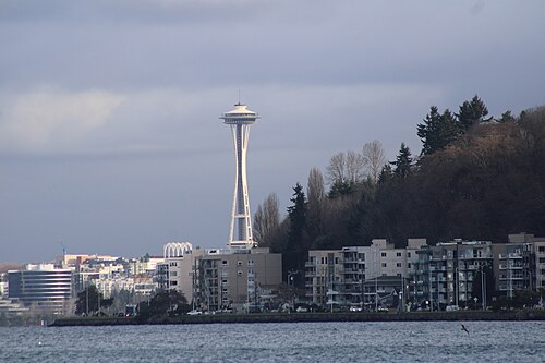 Mid rise waterfront apartment buildings along the Alki shoreline with the Space Needle and downtown Seattle rising across the water.