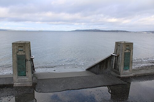 Concrete steps built into the seawall lead from the sidewalk down to the beach, a metal handrail between two square posts.