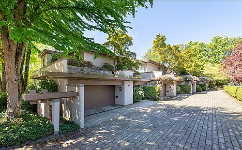 Modern stucco townhomes behind a gated brick paved driveway, balconies and clipped hedges along the front.