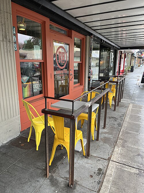 A cafe storefront numbered 403 with orange trimmed windows and a row of yellow chairs and tables set out under the awning on the sidewalk.