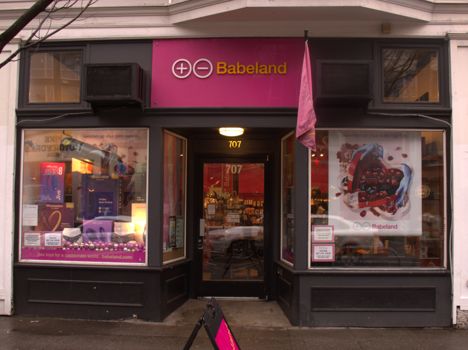 A ground floor storefront on Pike Street, dark paint with pink signage and lit window displays either side of the door.