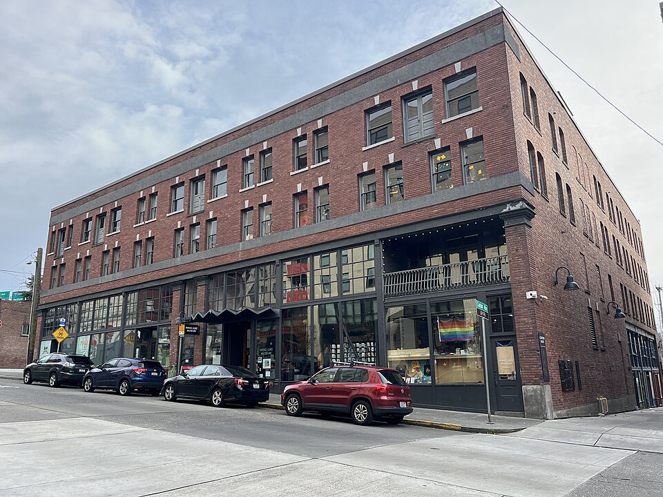 The Wing Luke Museum's storefront in the East Kong Yick Building on South King Street, large display windows and a recessed entrance under the awning, cars parked along the curb.